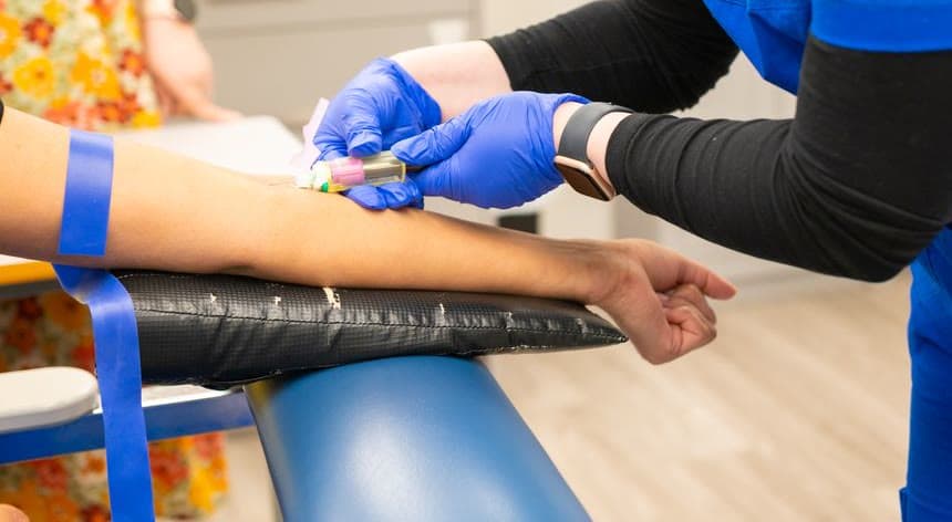A gloved healthcare worker draws blood from a patient's arm